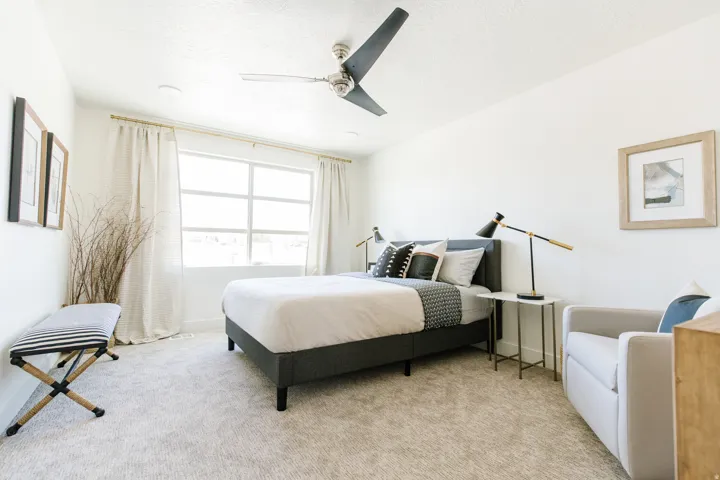 Bright interior space featuring a large window with white trim, a ceiling fan with dark blades, and light-toned wall-to-wall carpeting