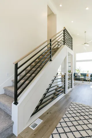 Modern staircase featuring black metal railings with a wood-finish handrail, carpeted treads, and white risers