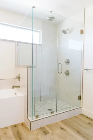 Glass-enclosed shower with a rainfall showerhead and secondary shower fixture, featuring light-toned tile walls and a mosaic tile shower pan