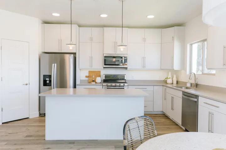 Modern kitchen featuring a central island, light wood-finish flooring, white cabinetry with brushed nickel hardware, and stainless steel appliances