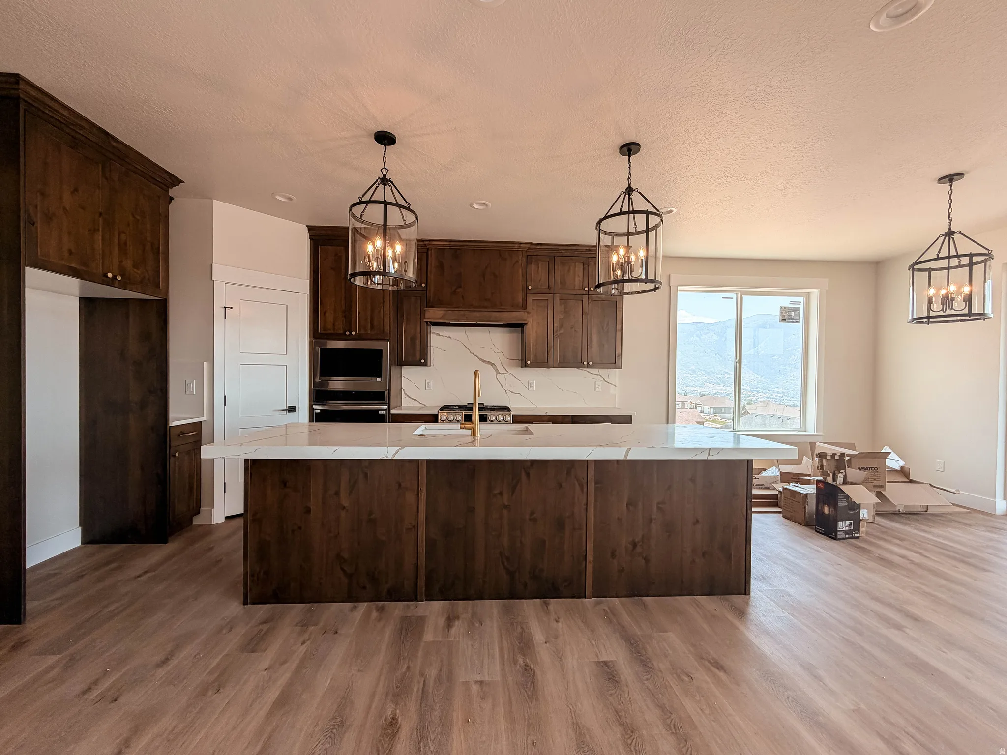 Spacious kitchen featuring dark wood cabinetry, a large center island with a light-toned countertop, and modern pendant lighting