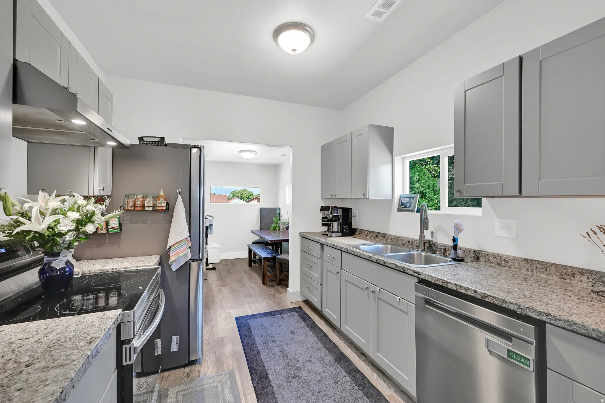 Kitchen featuring light gray cabinetry, stainless steel appliances, speckled countertops, wood-finish flooring, and a double basin sink