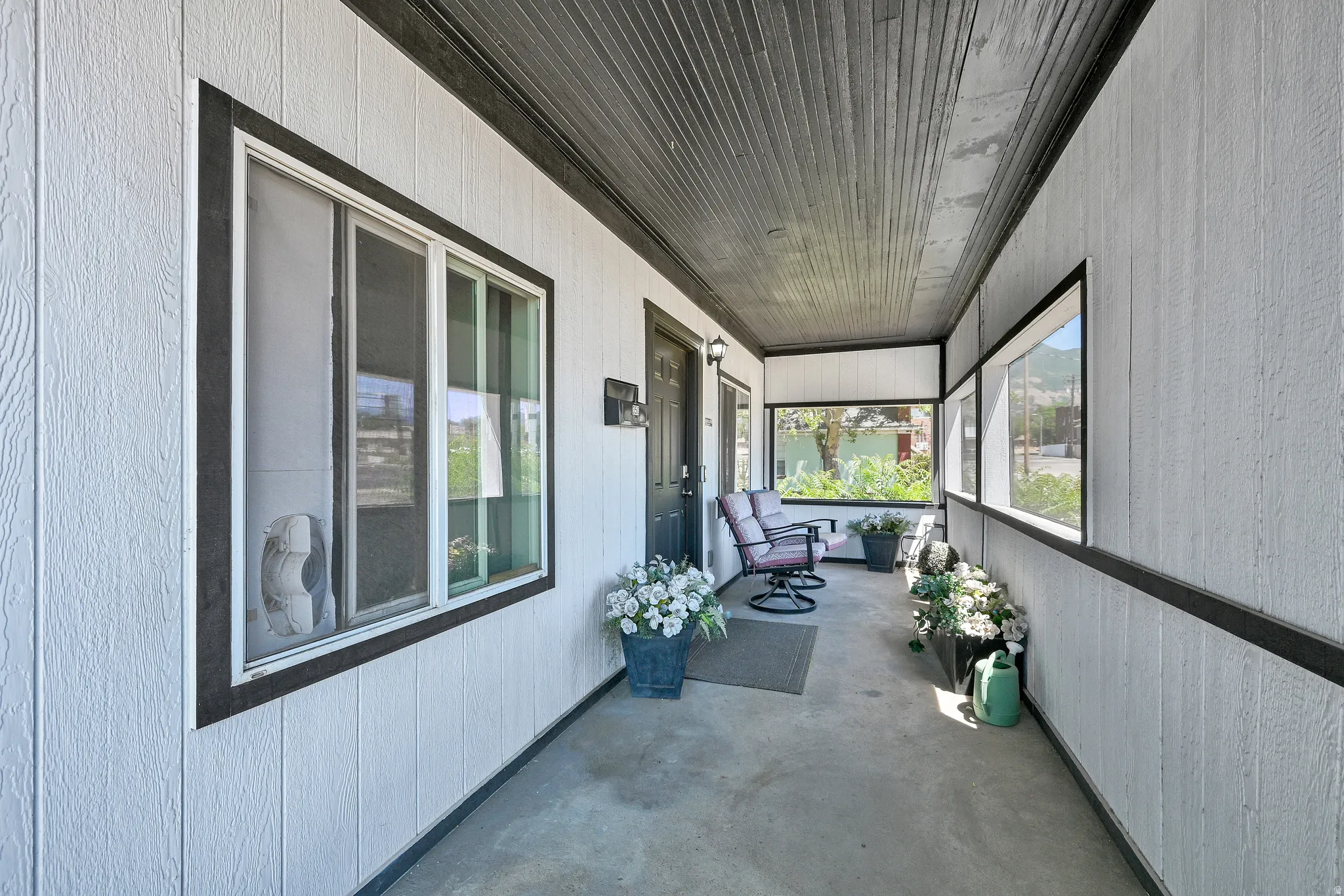 Covered porch featuring vertical white siding, black trim, a wood-finish ceiling, and concrete flooring