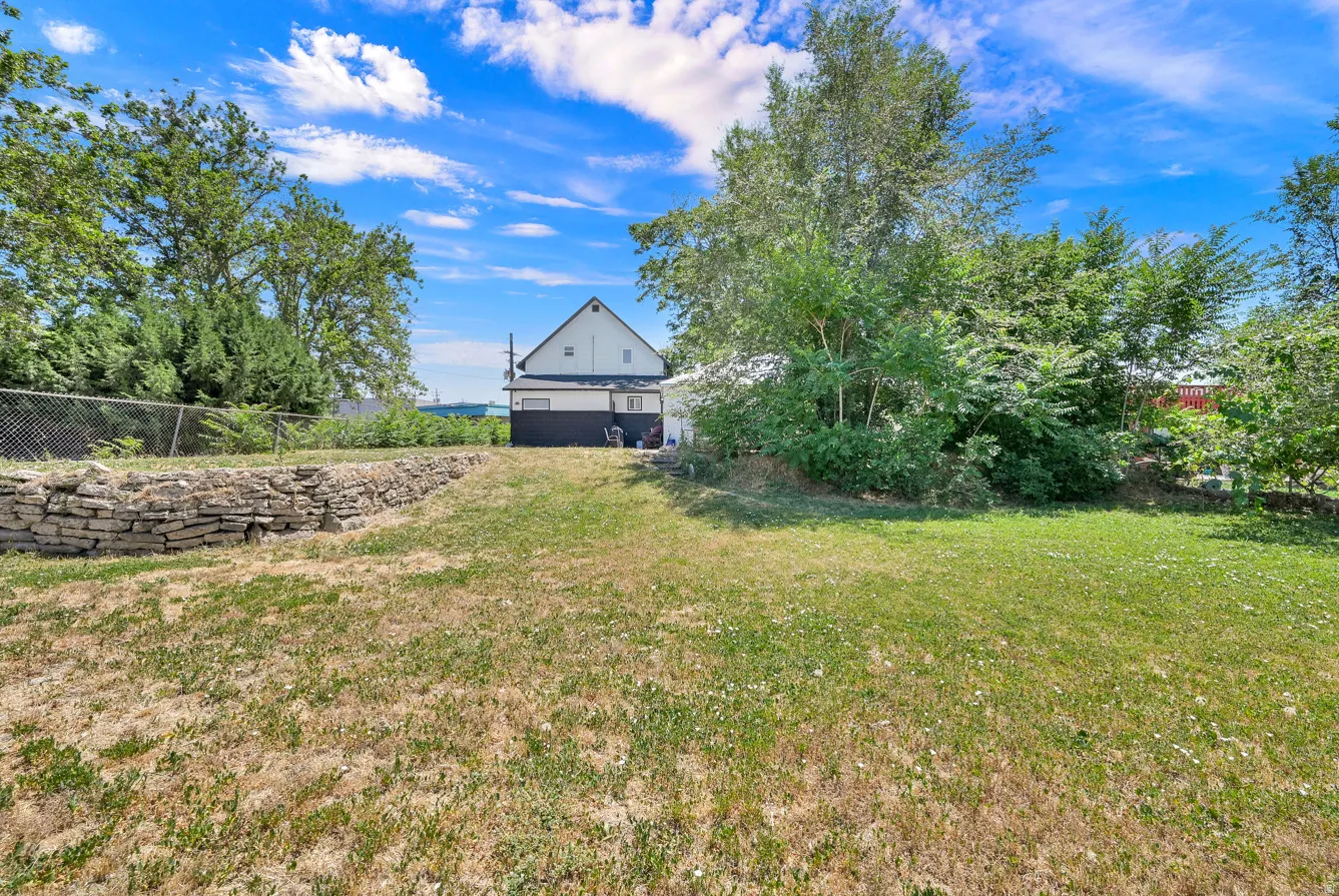 Expansive lawn area featuring a stone retaining wall and mature perimeter trees
