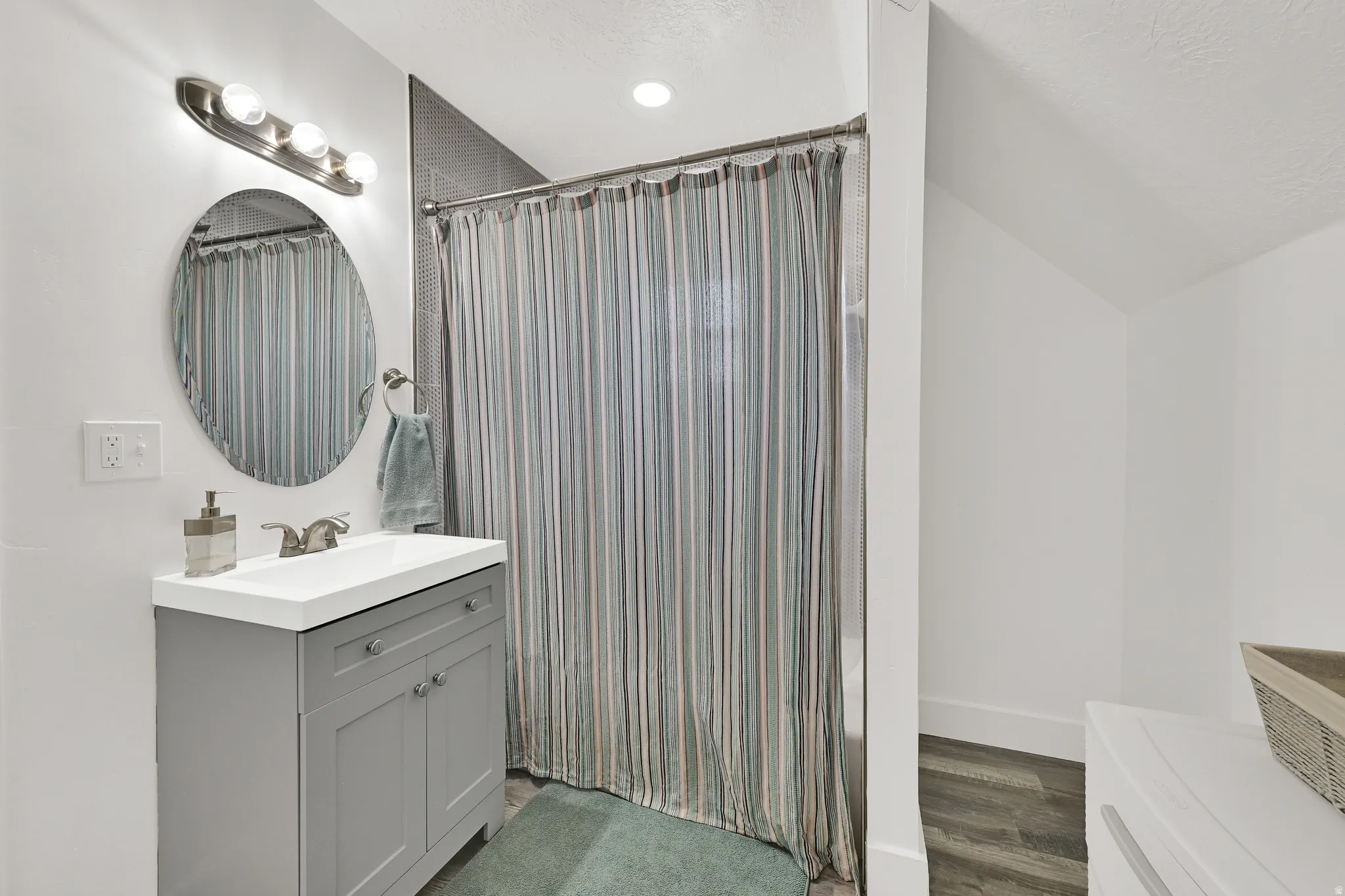 Bathroom featuring a gray vanity with an integrated white sink, an oval mirror, and brushed nickel fixtures