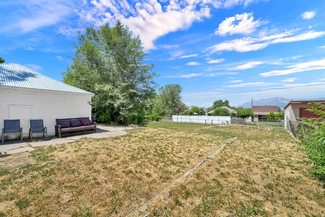 Expansive backyard featuring a large paved patio, mature trees, and a mountain backdrop