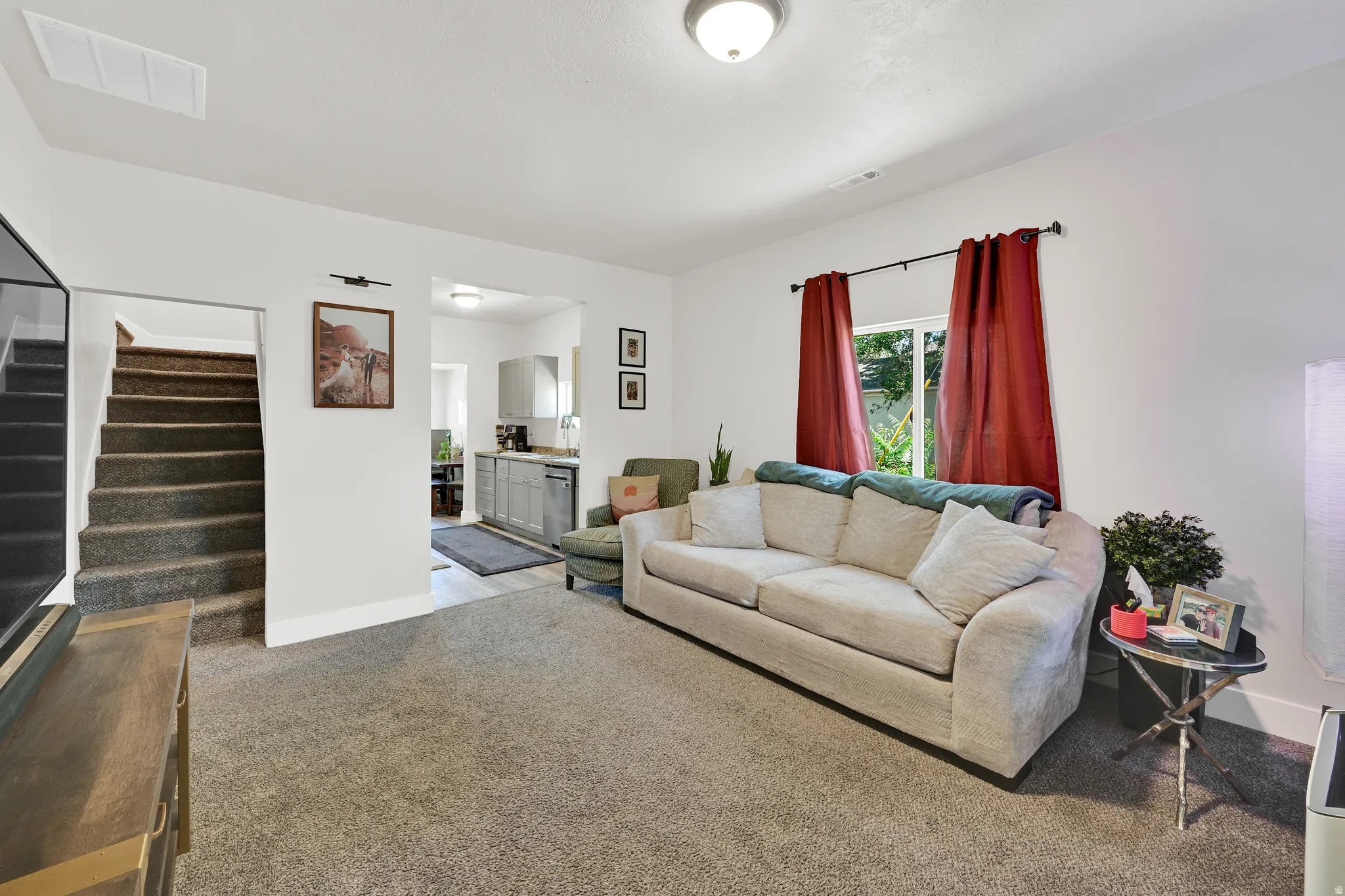 Carpeted living area featuring white walls, a window with dark curtain rods, and a ceiling-mounted light fixture