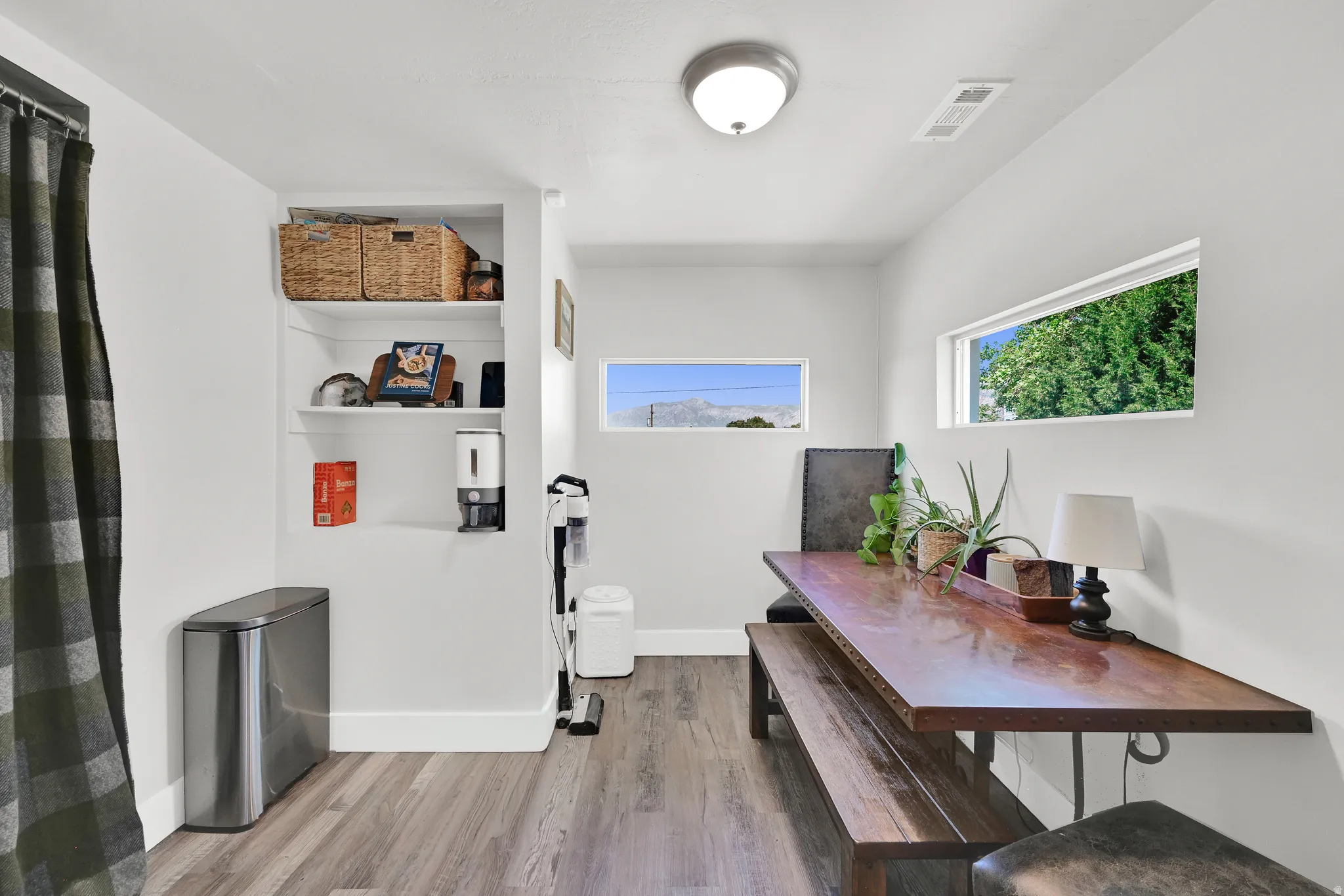 White wall interior with wood-finish flooring, two horizontal picture windows, and built-in shelving