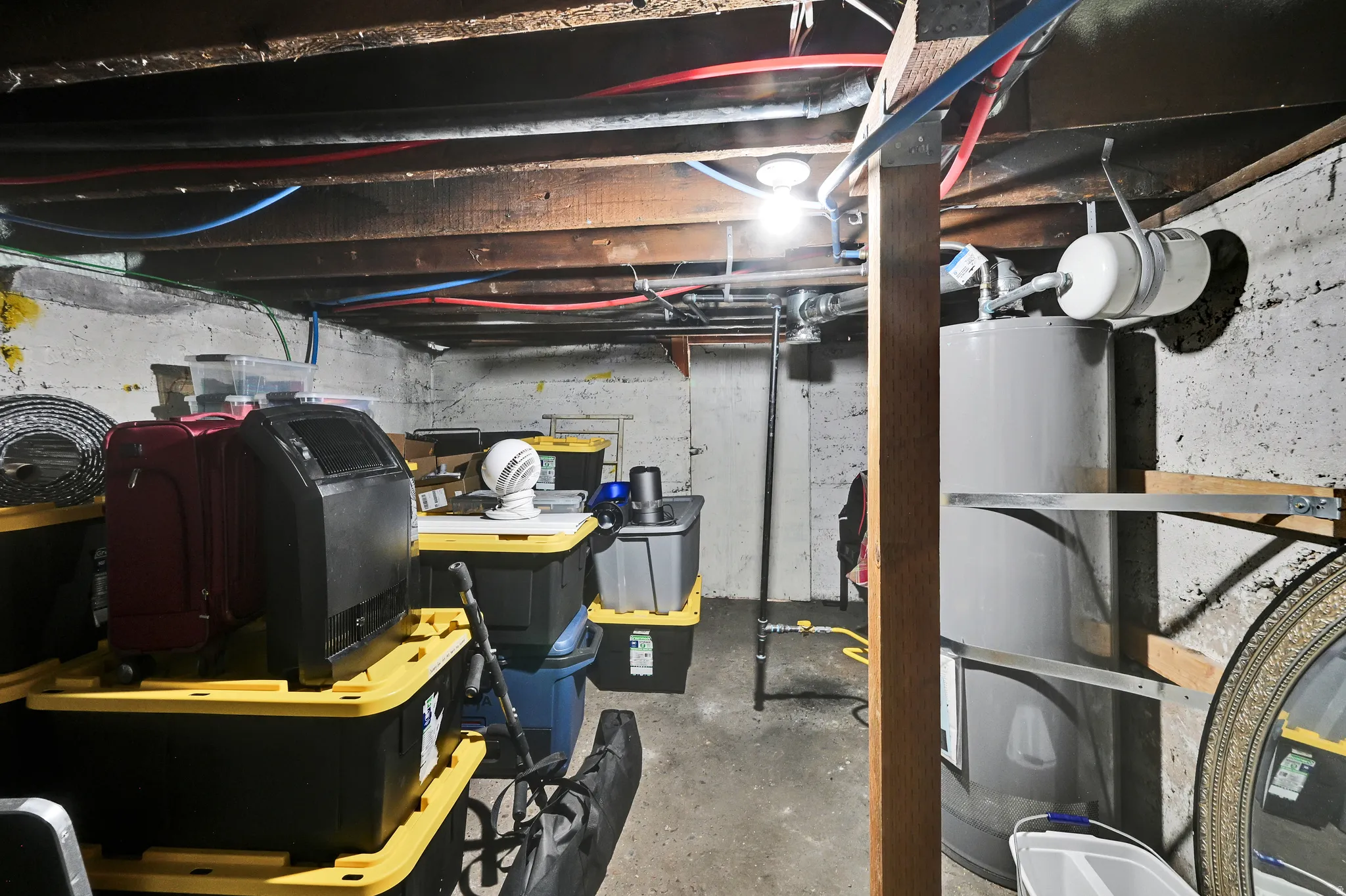 Utility basement featuring exposed wood joists, visible plumbing, a water heater, and concrete walls