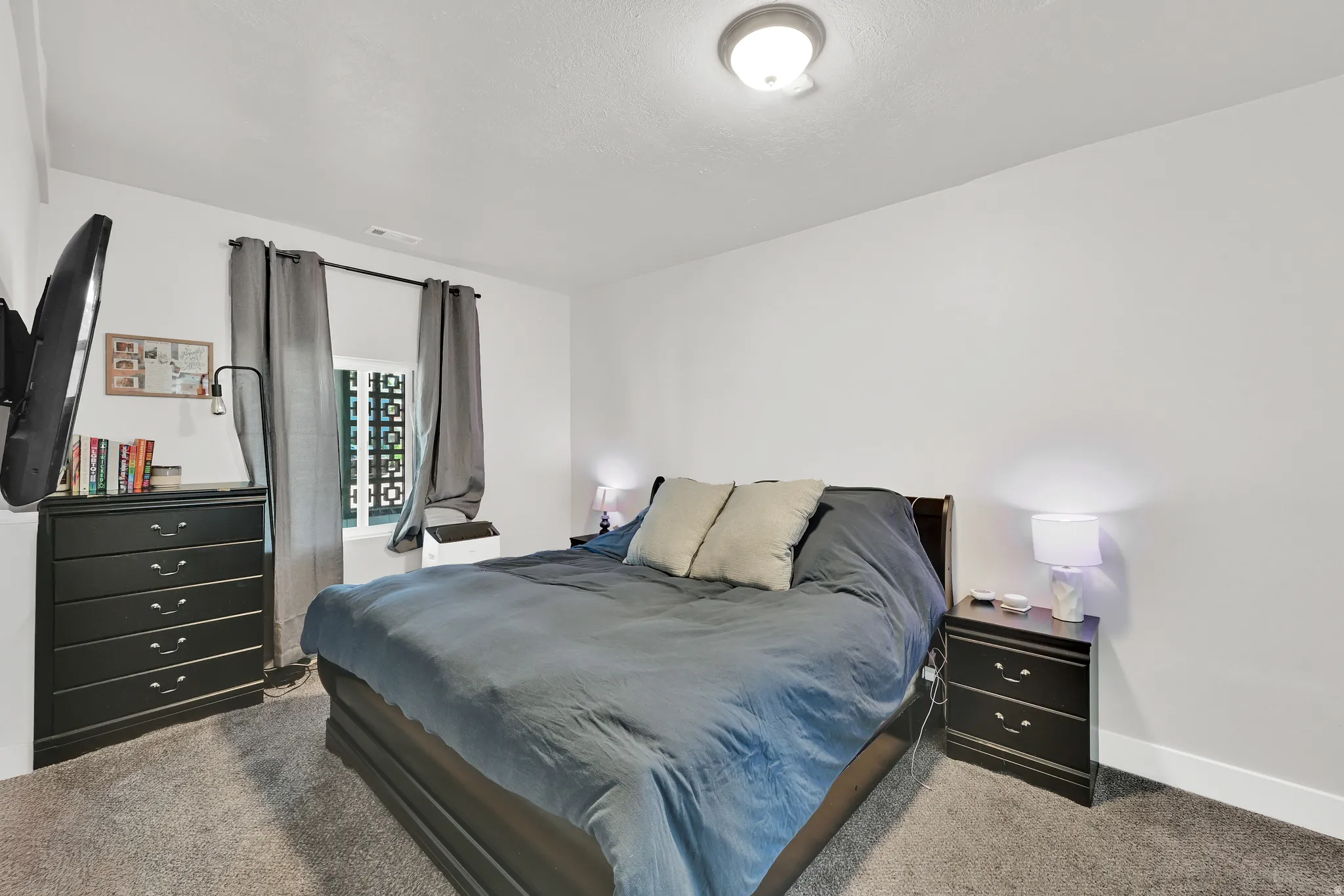Carpeted room featuring a window with decorative metalwork, white walls, and a ceiling-mounted light fixture