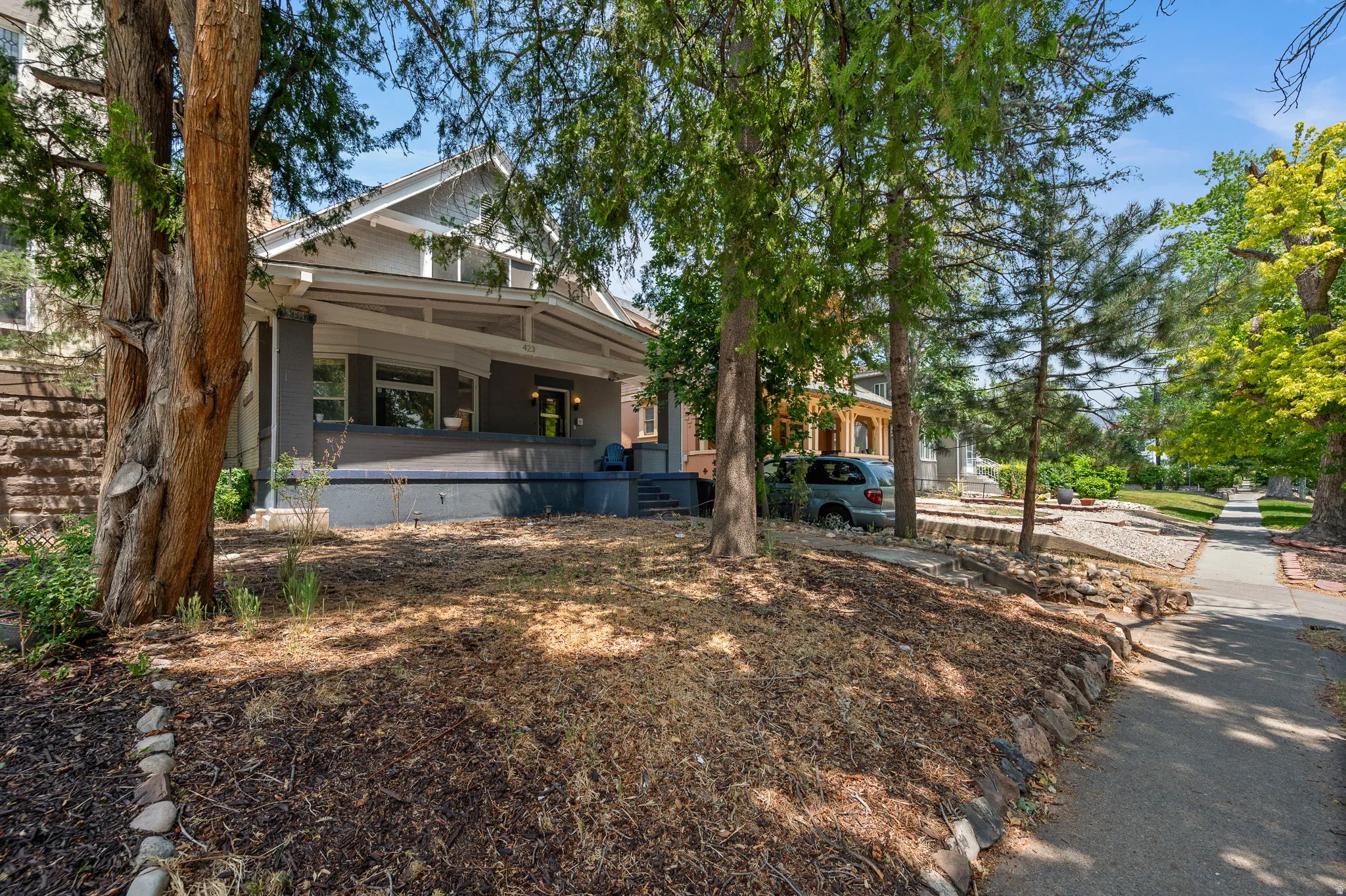 Craftsman-style home featuring a covered front porch with substantial columns, a gabled roofline, and multiple mature trees providing natural shade