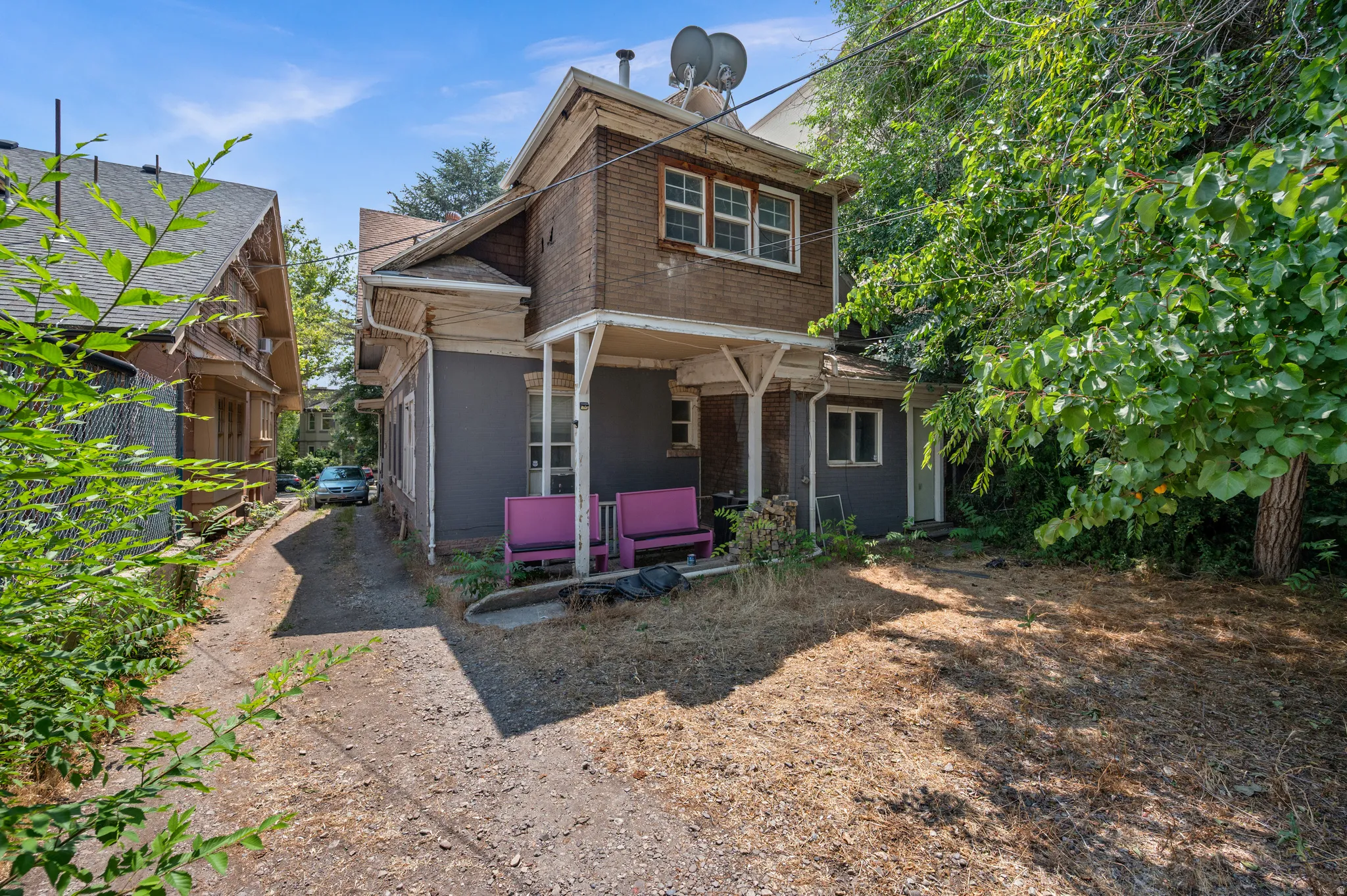 Brick-clad upper level with double-hung windows, a covered front porch, and a gravel driveway