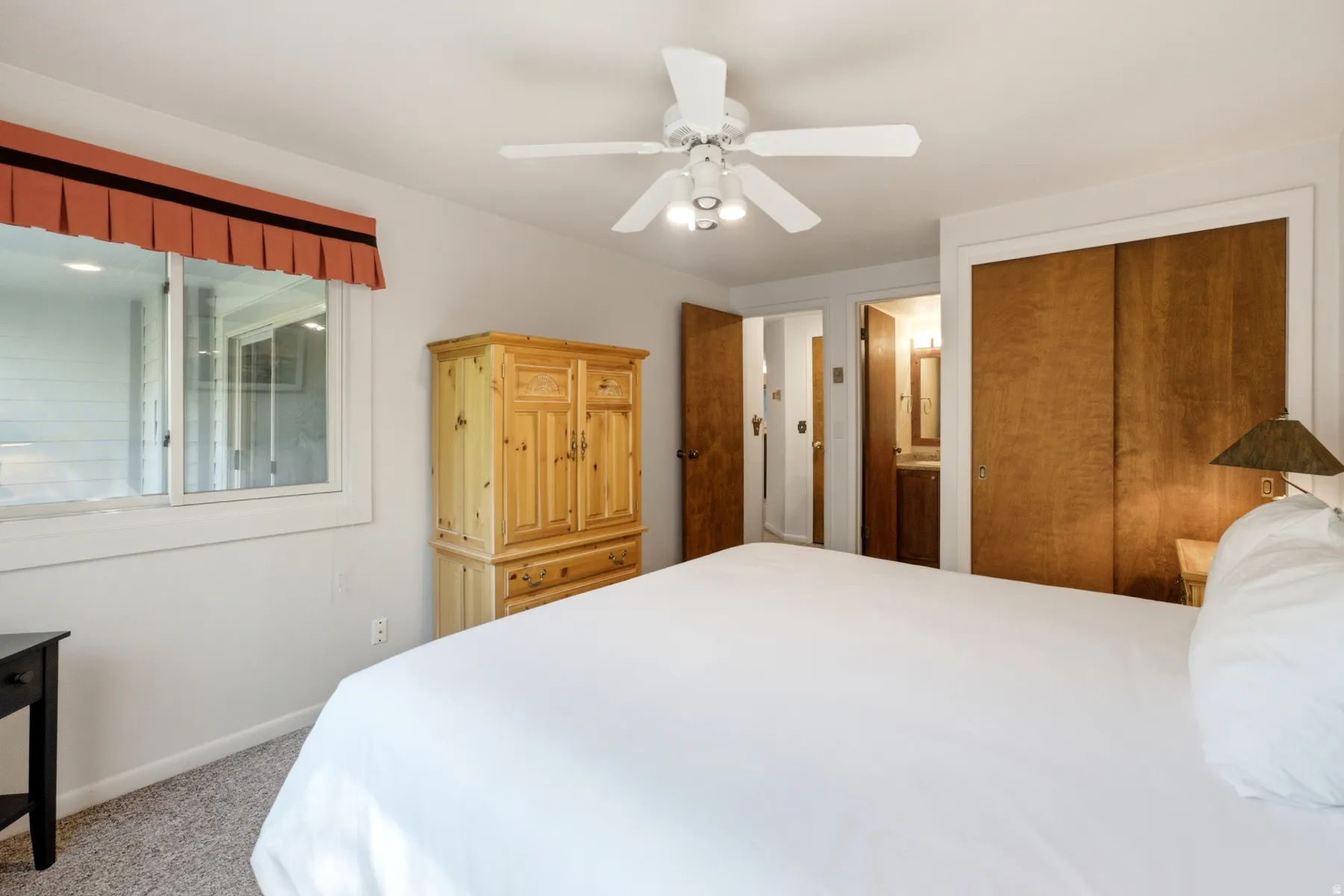 White ceiling fan with integrated lighting, wood-finish bi-fold closet doors, and light gray carpeted flooring