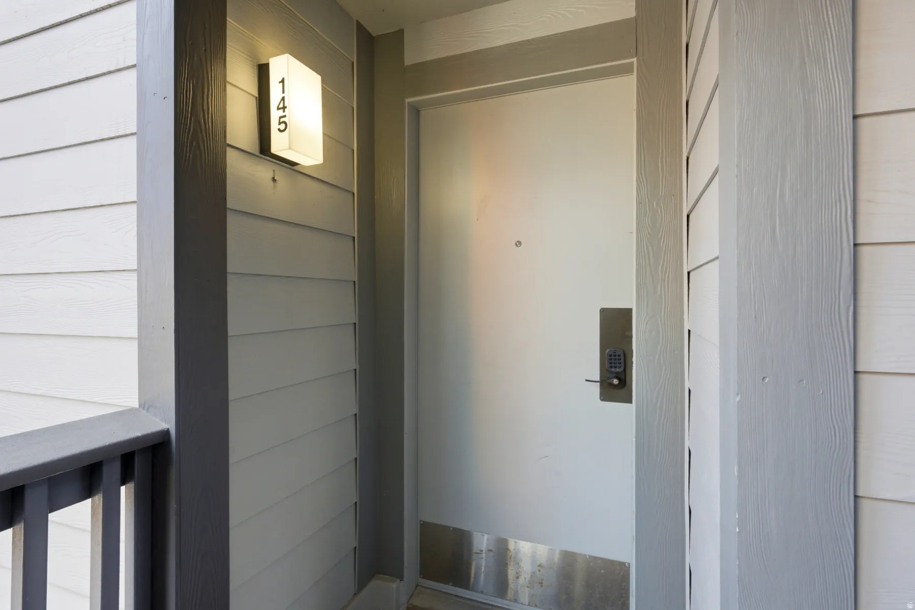 Entryway featuring light-colored horizontal siding, a contemporary wall sconce with address numbers, and a door with a keyless entry system