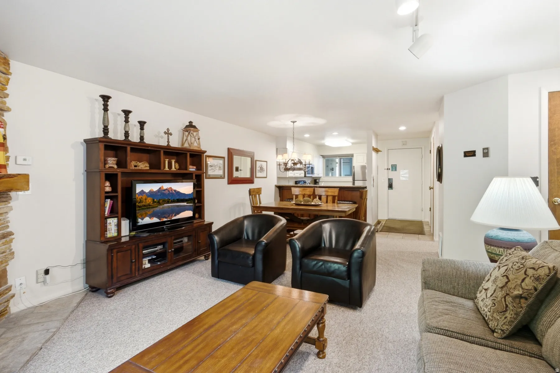Carpeted living area featuring a stone accent wall, built-in entertainment center, and a cased opening to the kitchen/dining area