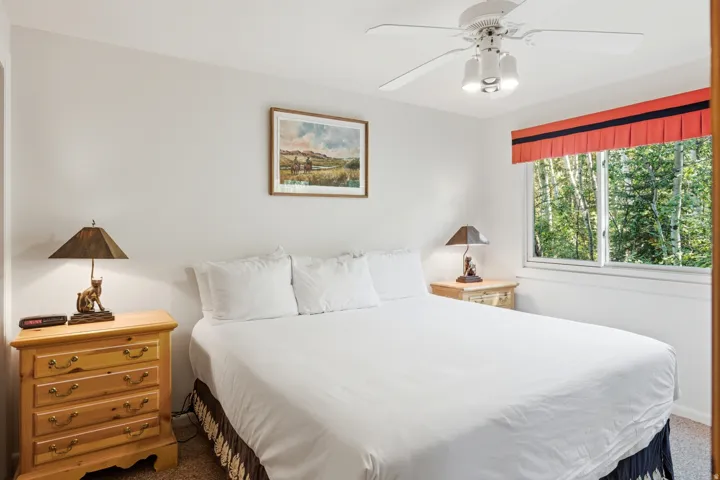 Bedroom featuring light-colored walls, a ceiling fan with integrated lighting, and a window with a green outdoor backdrop
