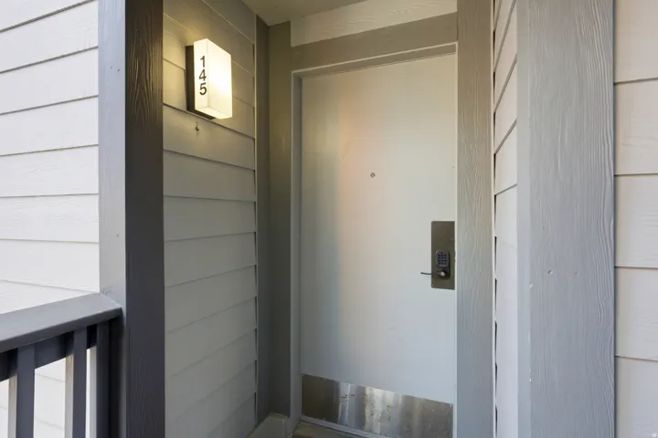 Entryway featuring light-colored horizontal siding, a contemporary wall sconce with address numbers, and a door with a keyless entry system