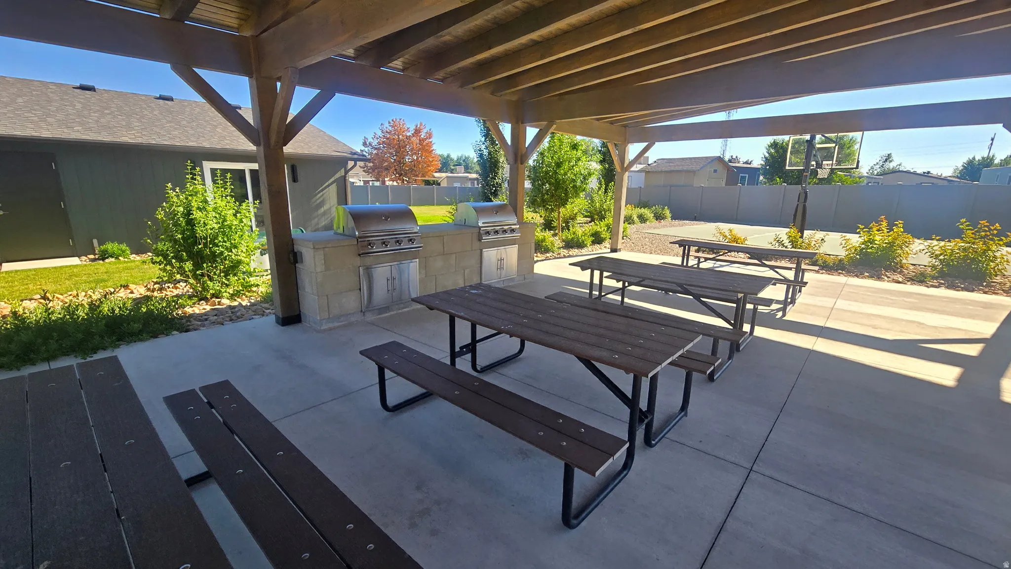 Covered outdoor patio with exposed beam pergola, dual built-in gas grills, stone-finish counter space, and multiple picnic tables