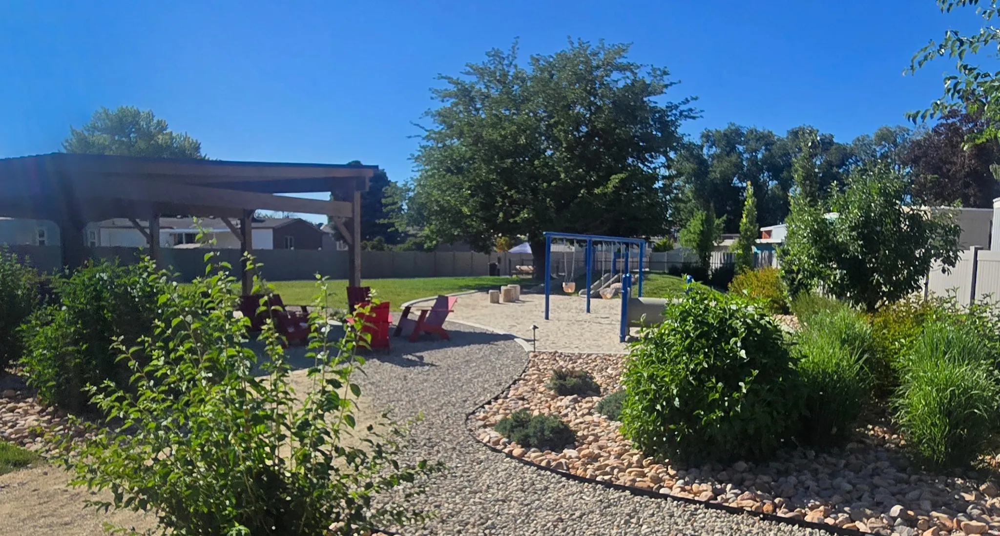 Expansive backyard featuring a gravel path, a wooden pergola, a lawn area, a swing set, and mature trees and shrubs