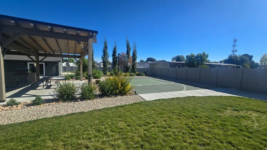 Expansive backyard featuring a covered patio, concrete paving, a manicured lawn, and a sport court