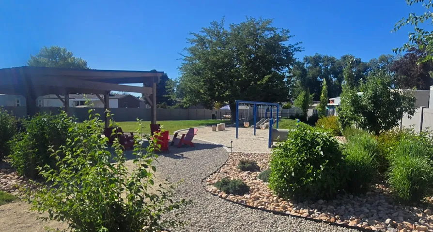 Expansive backyard featuring a gravel path, a wooden pergola, a lawn area, a swing set, and mature trees and shrubs