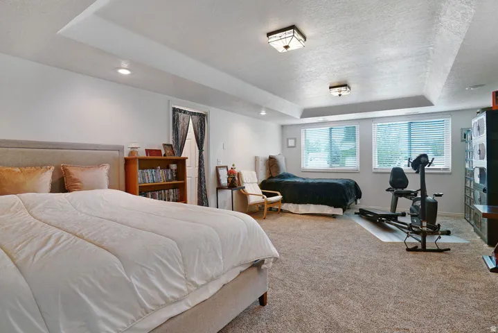 Spacious room featuring tray ceilings with recessed lighting and flush-mount fixtures, two windows with blinds, and neutral carpeting