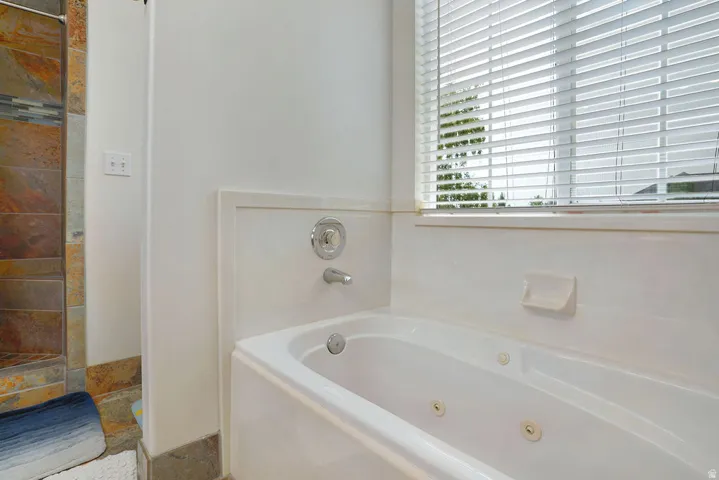 Jetted soaking tub with chrome fixtures, complemented by a tiled shower surround featuring earth-toned stone and a decorative glass tile accent band