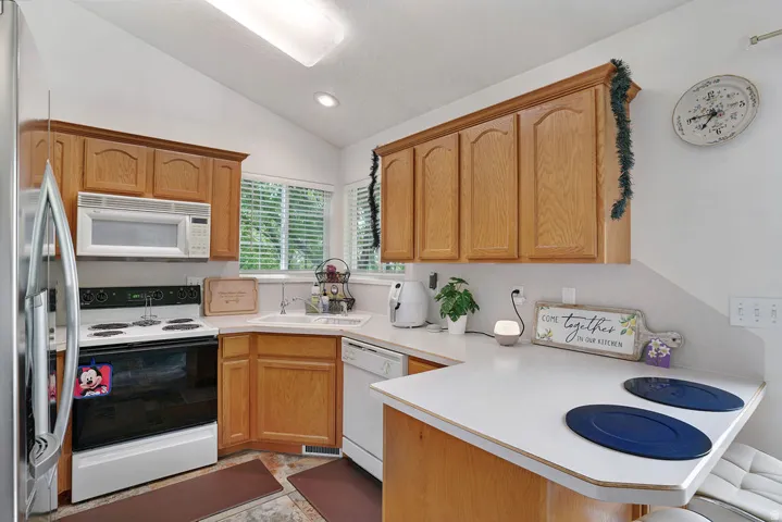 Kitchen featuring wood-finish cabinetry, white countertops, built-in microwave, stainless steel refrigerator, and a corner sink with a window