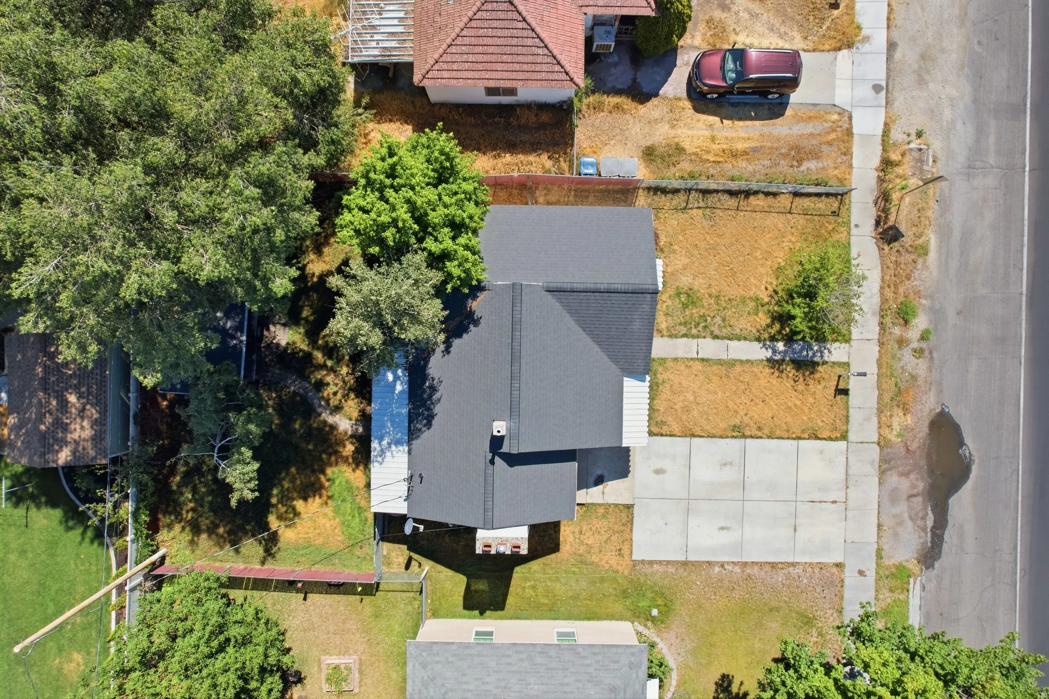 Aerial perspective showcasing a property with a dark shingle roof, mature trees, and a concrete driveway