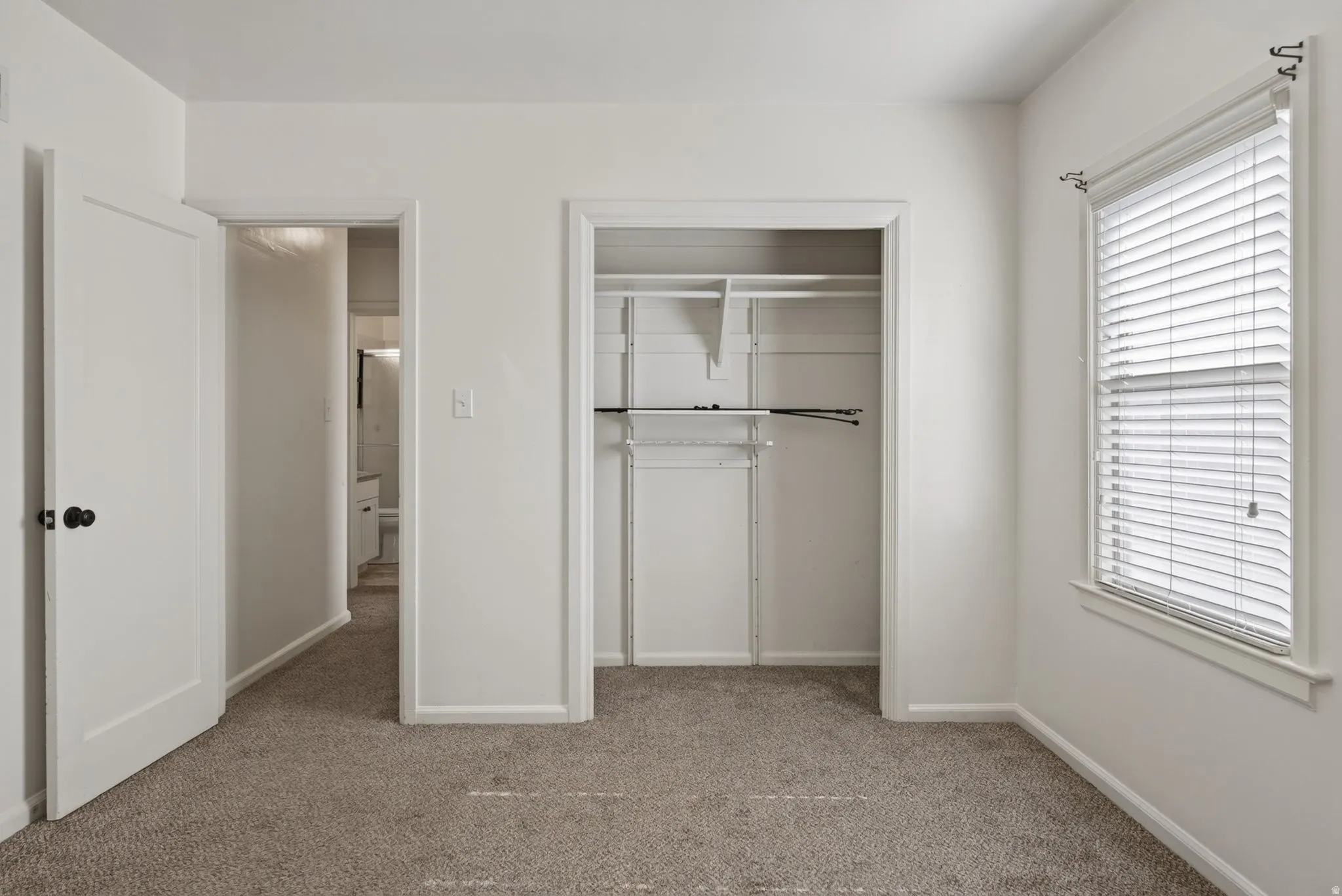 Carpeted room with white walls, featuring a built-in closet with shelving and hanging rods