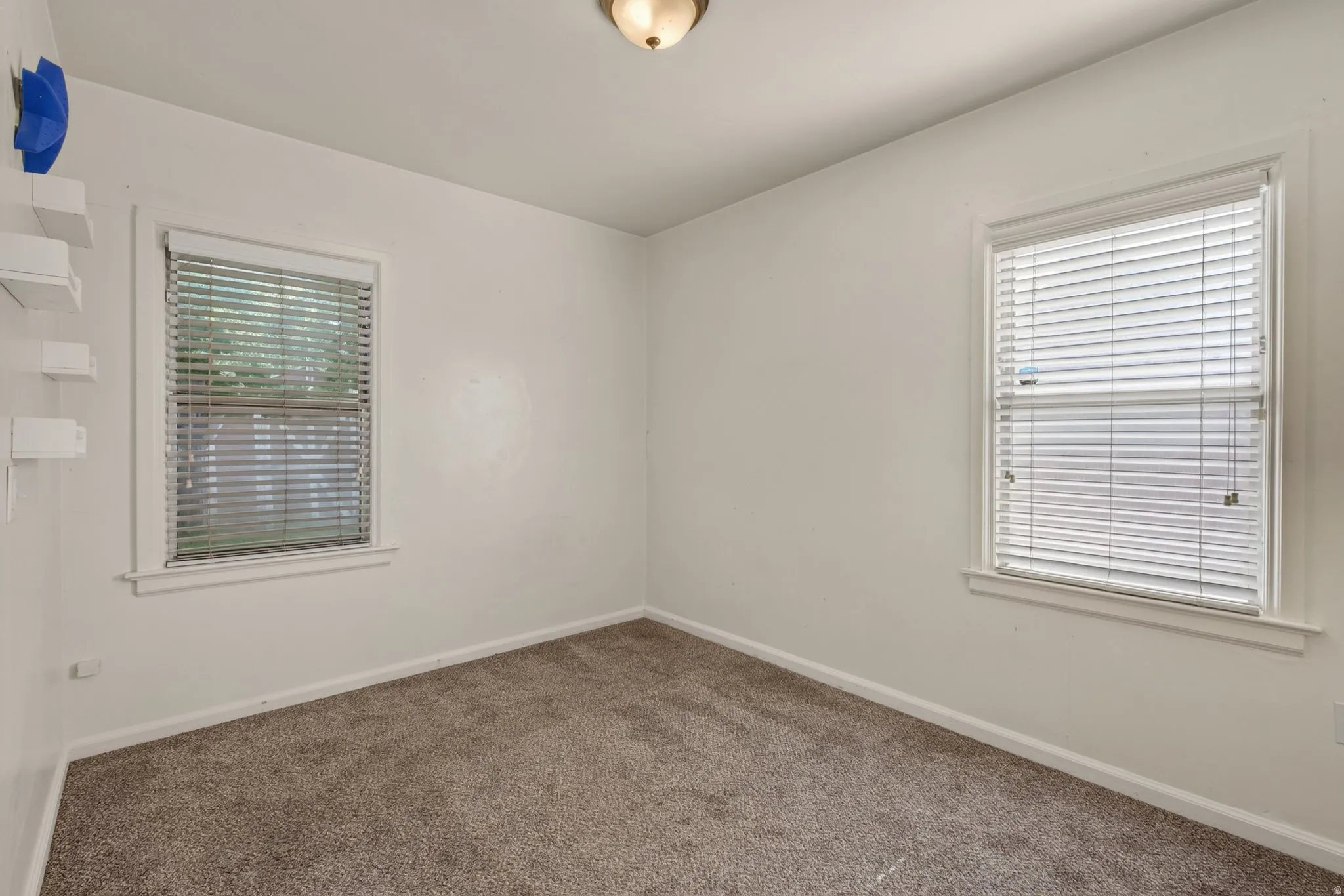 Room featuring two windows with horizontal blinds, neutral wall paint, and carpet flooring