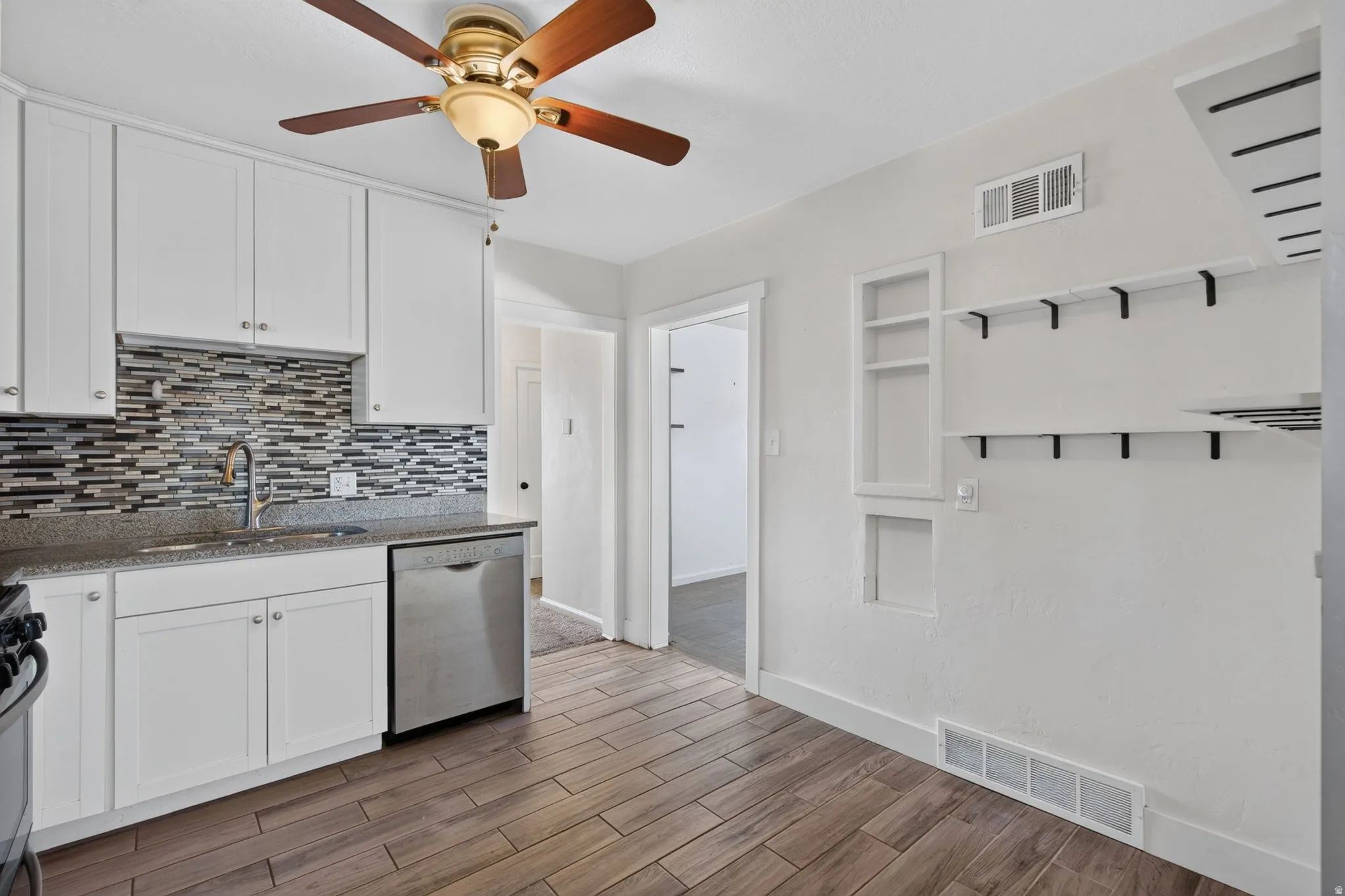 Kitchen featuring white cabinetry, a mosaic tile backsplash, wood-finish flooring, a stainless steel dishwasher, and a ceiling fan with integrated lighting