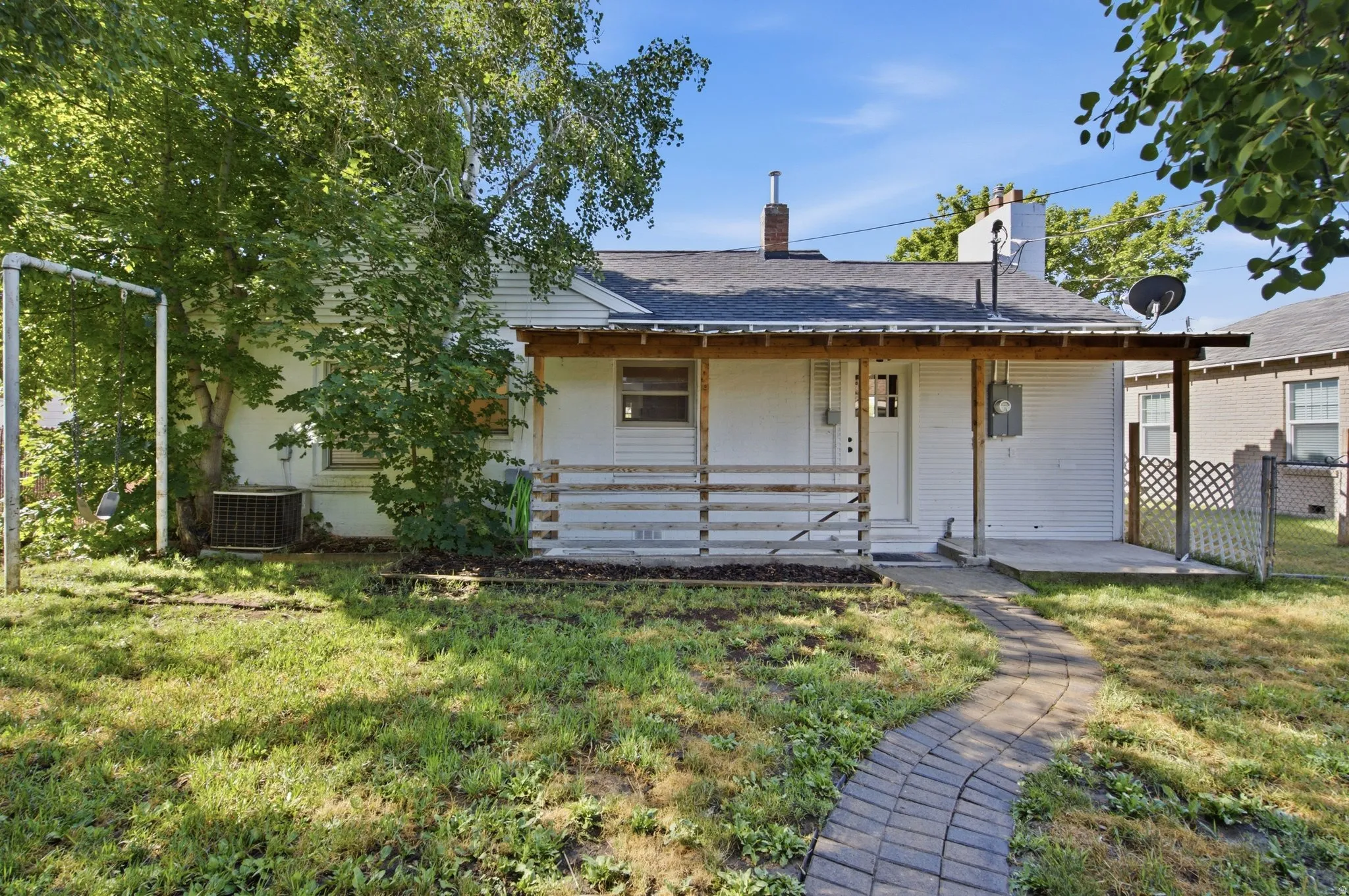 White exterior featuring a covered porch, wood porch railings, and a brick pathway