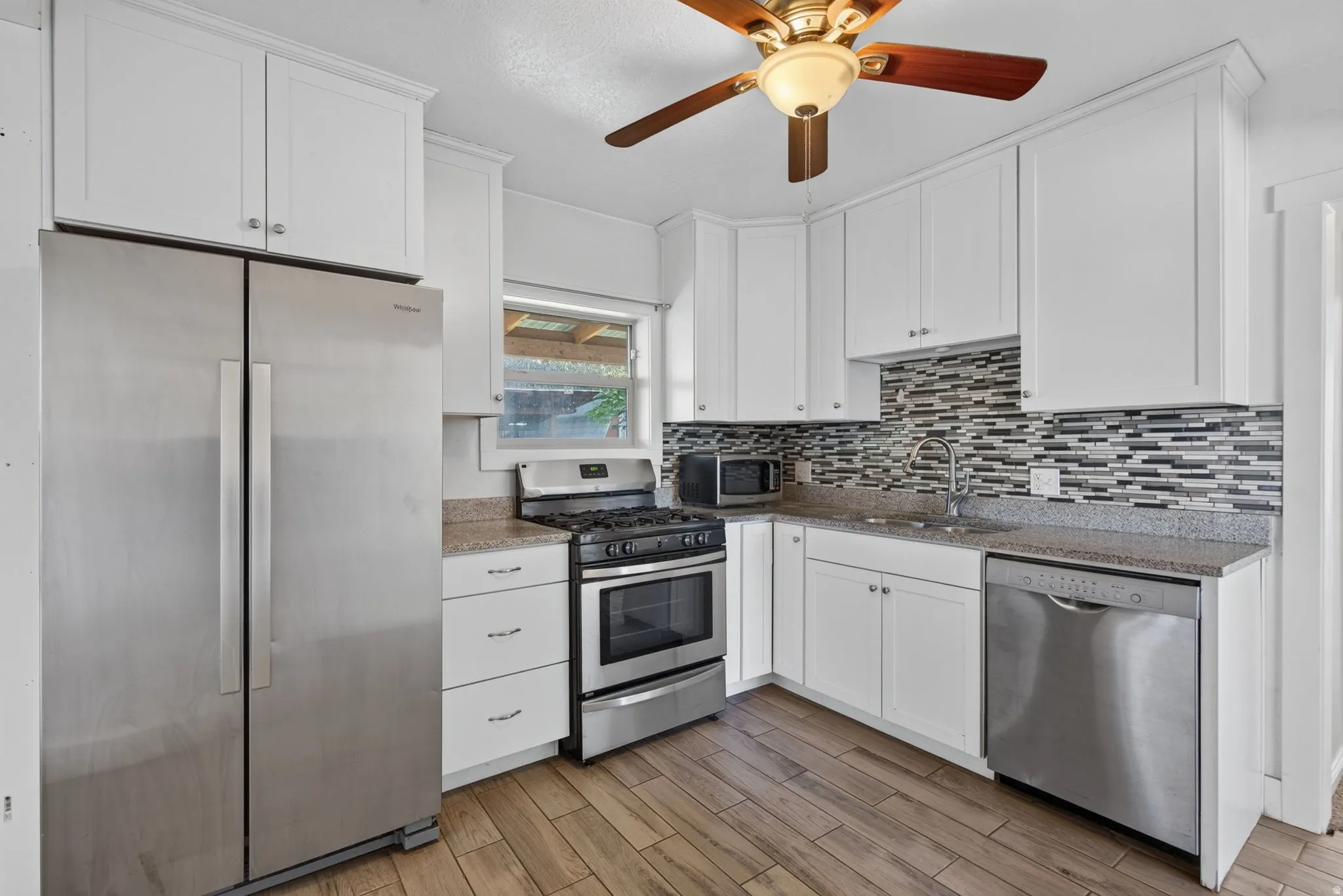 Kitchen featuring wood-finish flooring, white cabinetry, a mosaic tile backsplash, and stainless steel appliances including a refrigerator, range, and dishwasher