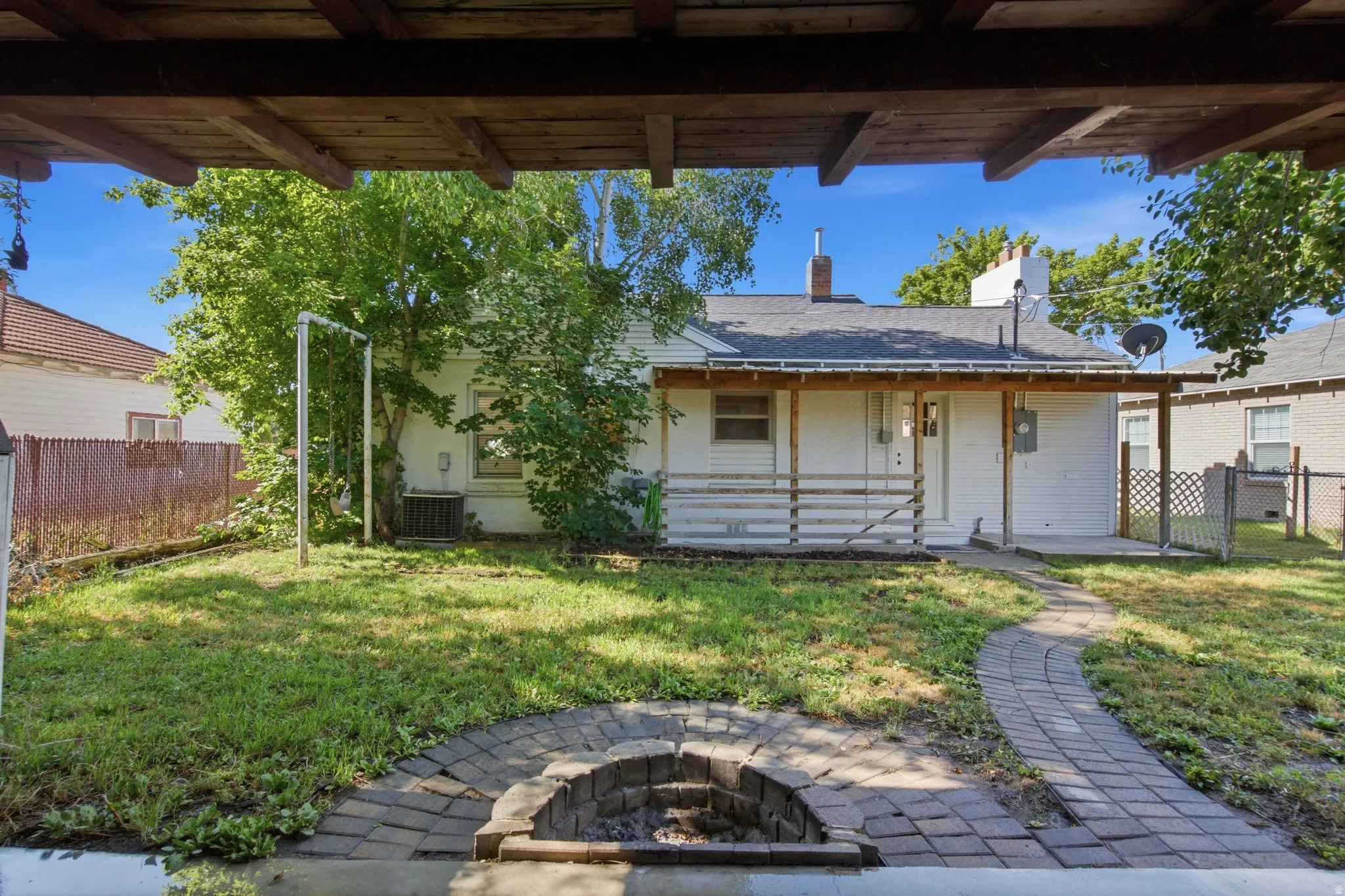Rear exterior featuring a covered porch with railing, a paved pathway, and a stone-lined fire pit