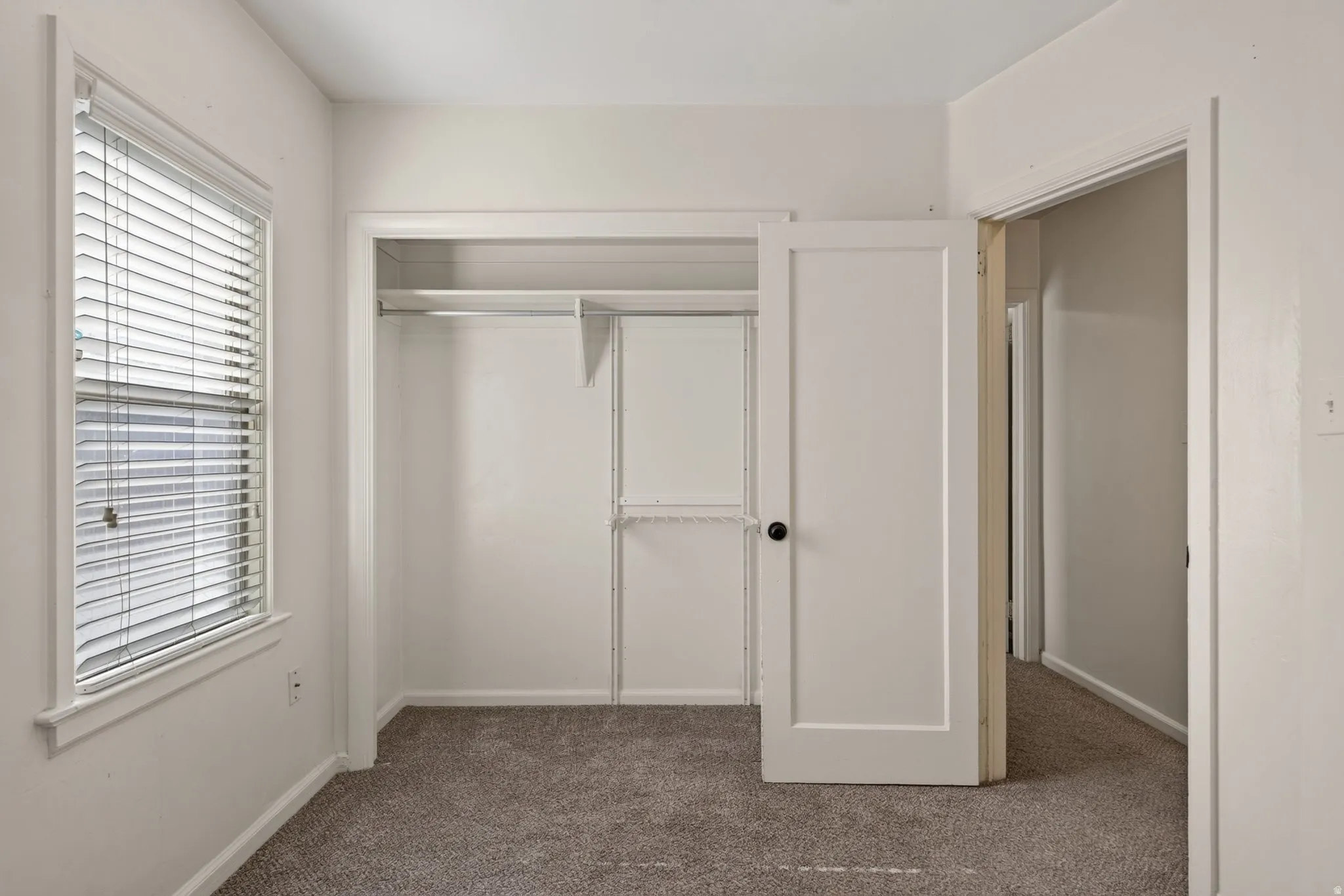 Bedroom featuring plush carpeting, a window with horizontal blinds, and a built-in closet with shelving and hanging rods