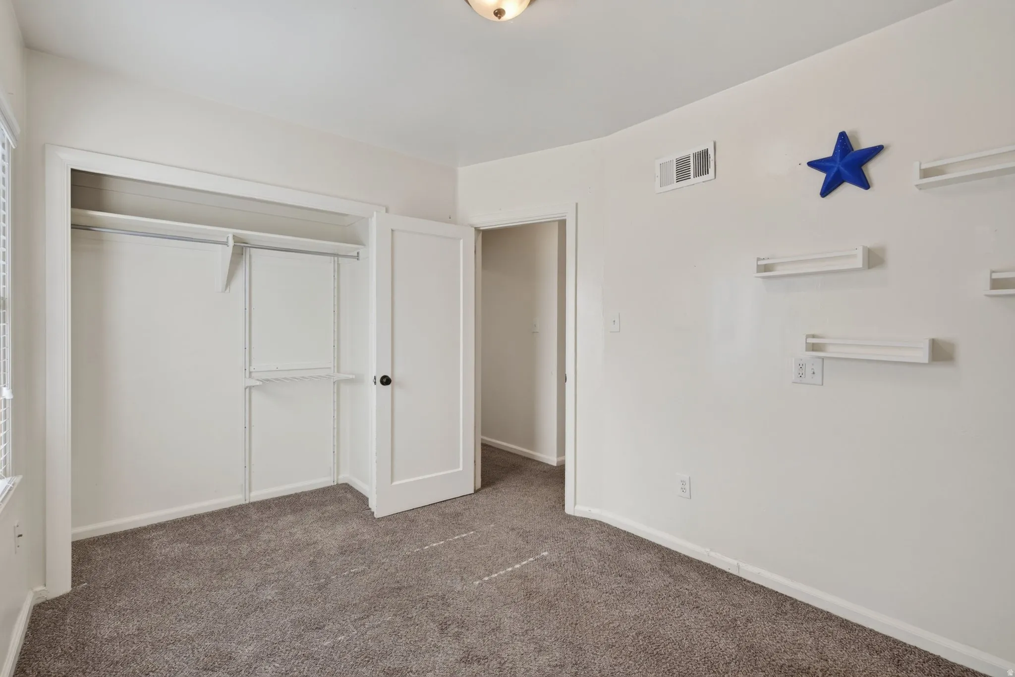 Carpeted room featuring a double-door closet with shelving and hanging rods, a single pane window with blinds, and white walls
