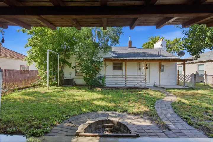 Rear exterior featuring a covered porch with railing, a paved pathway, and a stone-lined fire pit