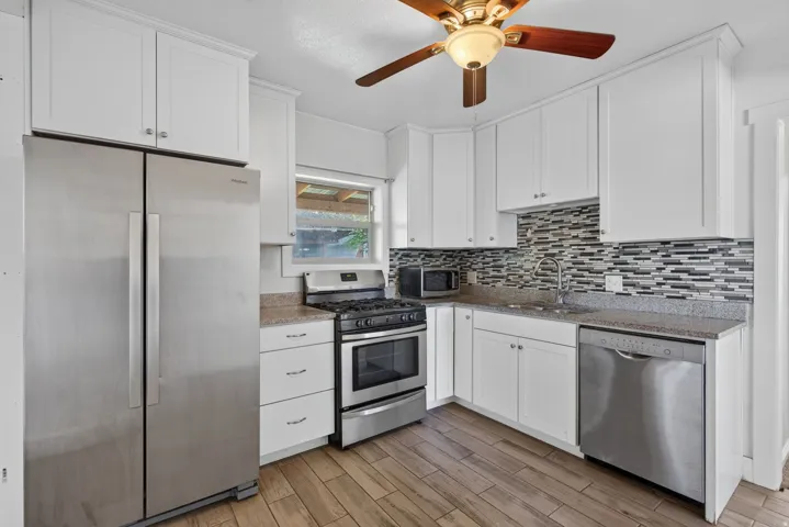 Kitchen featuring wood-finish flooring, white cabinetry, a mosaic tile backsplash, and stainless steel appliances including a refrigerator, range, and dishwasher