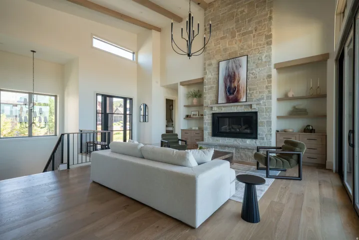 Great room featuring a stone fireplace with a wood mantel, built-in shelving, wood-finish flooring, and exposed ceiling beams