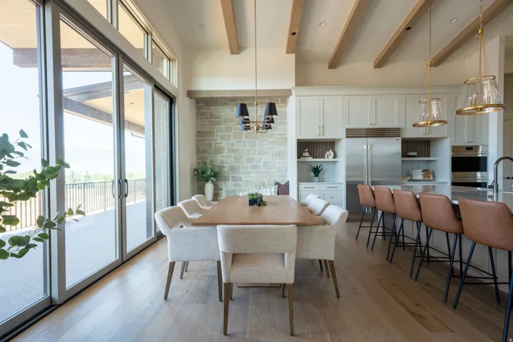 Extensive sliding glass doors, wood-finish flooring, exposed ceiling beams, a stone accent wall, and built-in stainless steel appliances