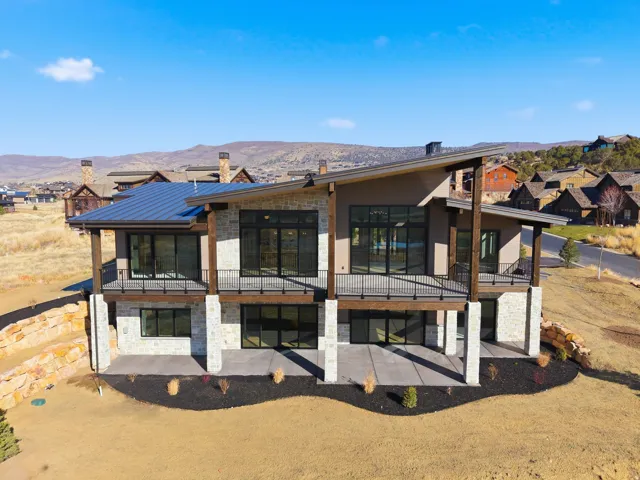 Contemporary architecture with stone and stucco exterior, prominent balcony with metal railing, and a sloped metal roof