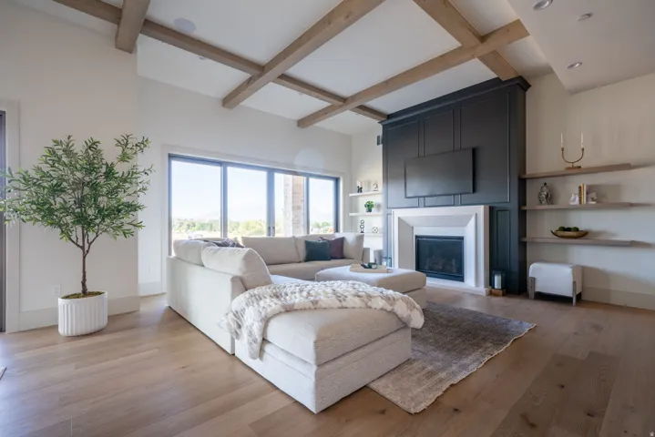 Vaulted ceiling with exposed wood beams, expansive windows, wood-finish flooring, built-in fireplace with mantel, and built-in shelving