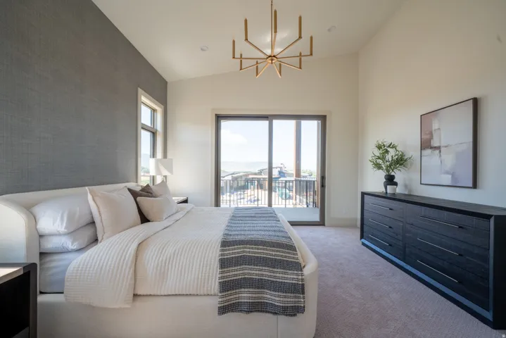 Vaulted ceilings with a brass chandelier, textured accent wall, and sliding glass door to a private balcony