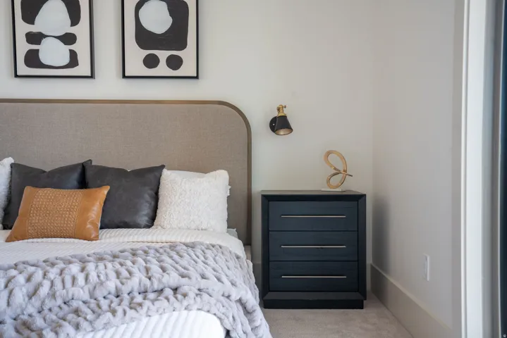 Upholstered headboard with rounded edges, matte black nightstand with three drawers, and a wall-mounted sconce with a brass accent