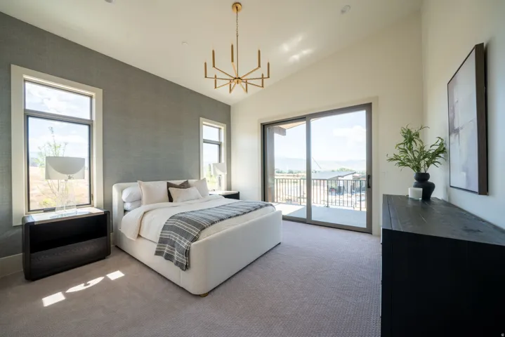 Vaulted ceiling with an angular chandelier, carpeted flooring, full-height sliding glass doors, and dual vertical windows