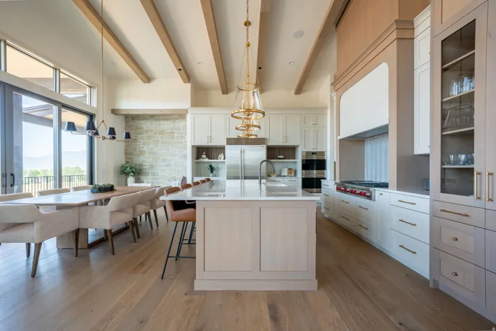 Wood-finish flooring throughout, kitchen island with built-in sink, vaulted ceilings with exposed wood beams, built-in dual ovens, and stone accent wall