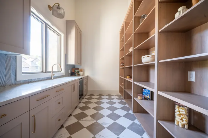 Extensive custom built-in shelving, checkered tile flooring, light-toned cabinetry, substantial window with natural light, and a dedicated beverage refrigerator