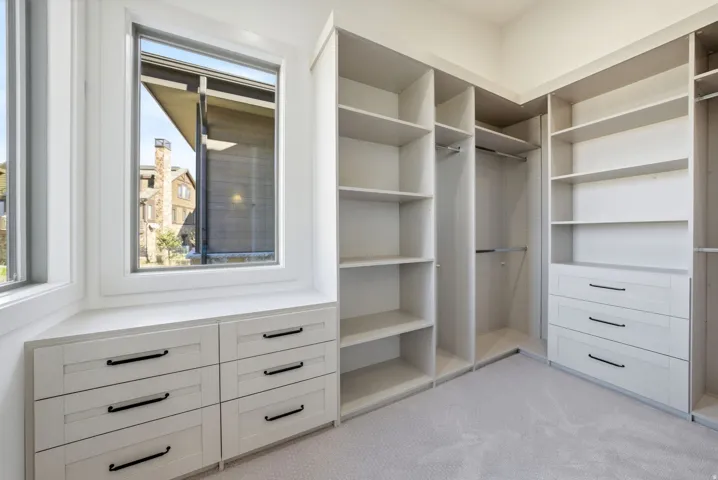Built-in custom cabinetry with shelving and drawers, ample hanging space, and a window with a built-in bench