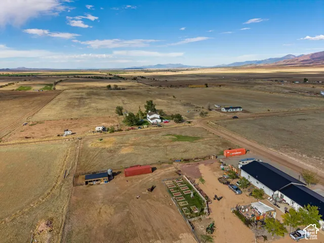 Aerial view of expansive acreage featuring open pasture land, a detached multi-purpose structure with a metal roof, and mountainous surroundings